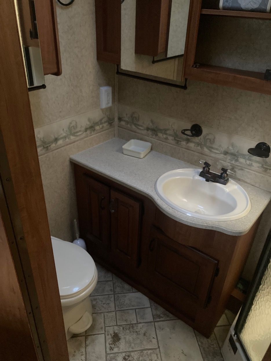 Bathroom in an RV, featuring a toilet, sink, vanity, and overhead cabinet with a mirror.