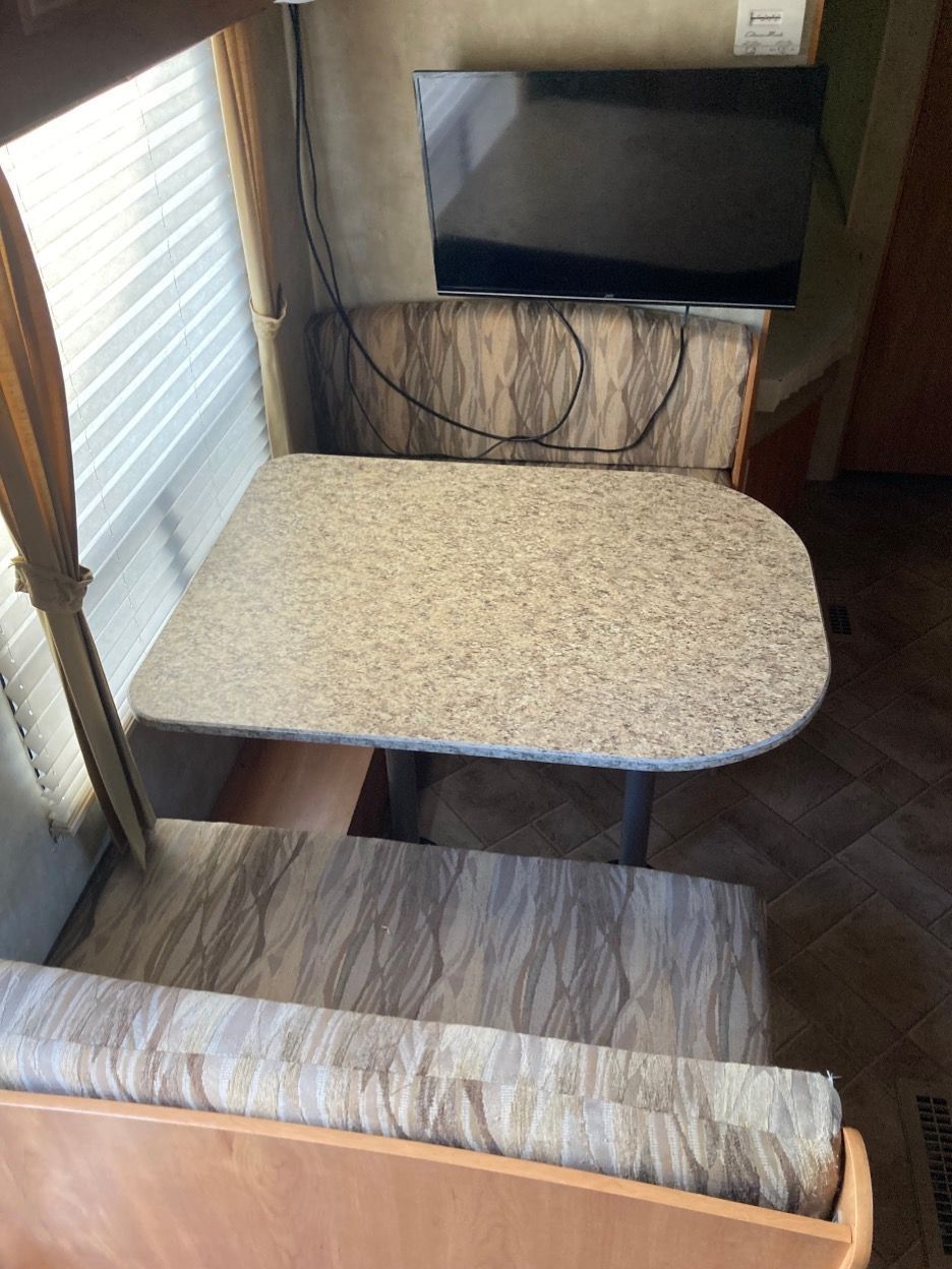 RV dining area with a table and bench seating, small TV mounted on the wall.