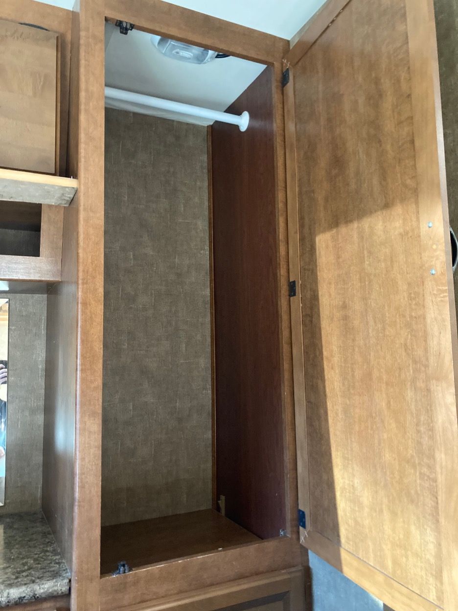 Empty RV closet with clothes rod and open wooden door.