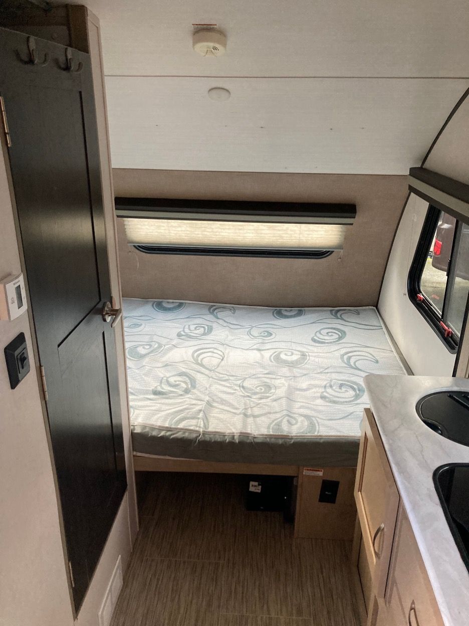 Interior view of a small RV, featuring a bed, window, and small kitchen area.