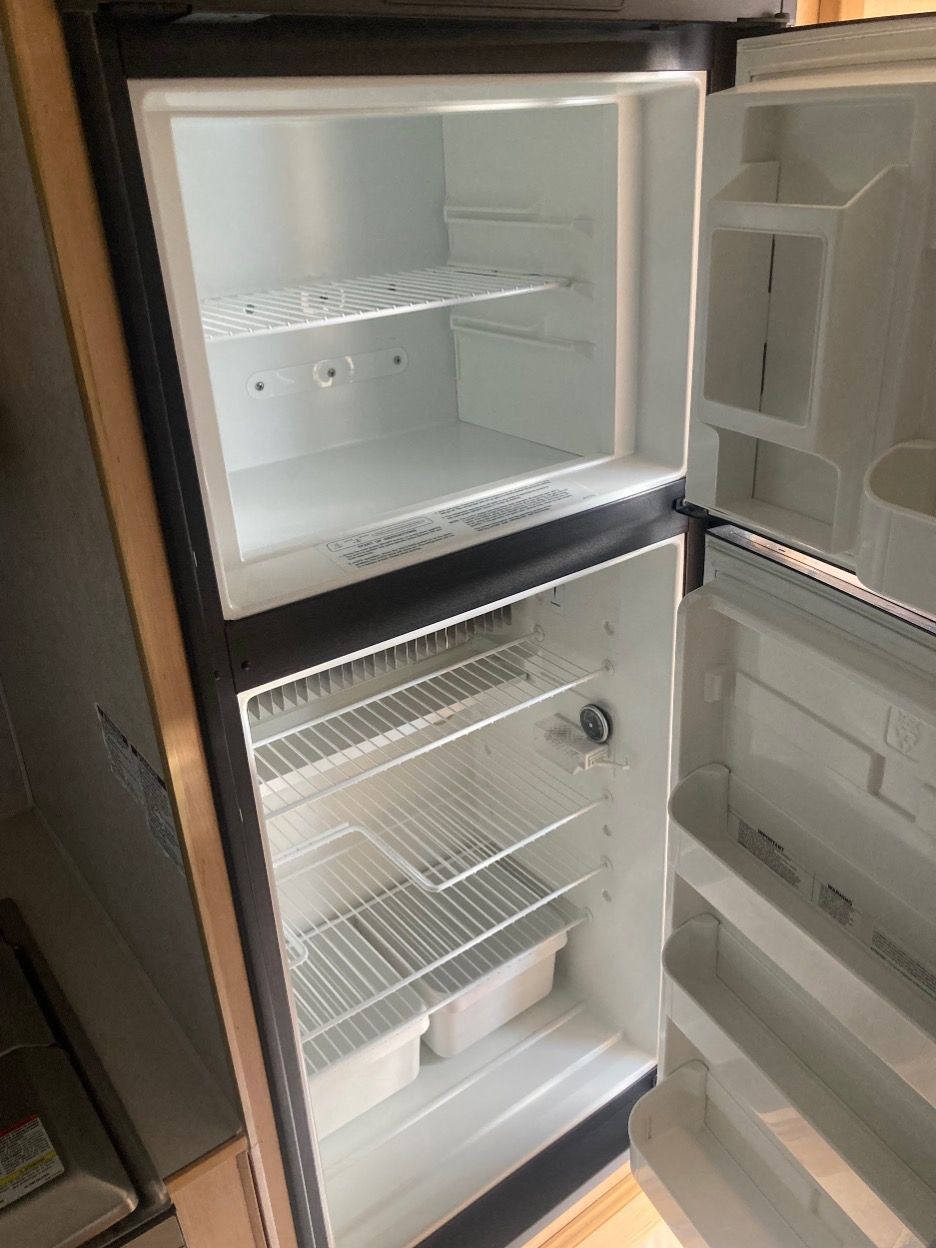 An open, empty, two-door refrigerator with a freezer on top. White interior with wire shelves.