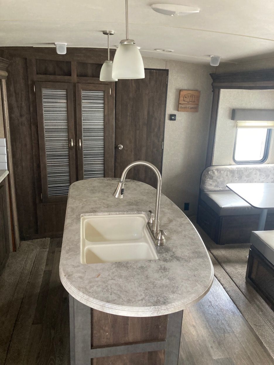 RV interior with kitchen island, sink, overhead lighting, cabinets, and a dinette.