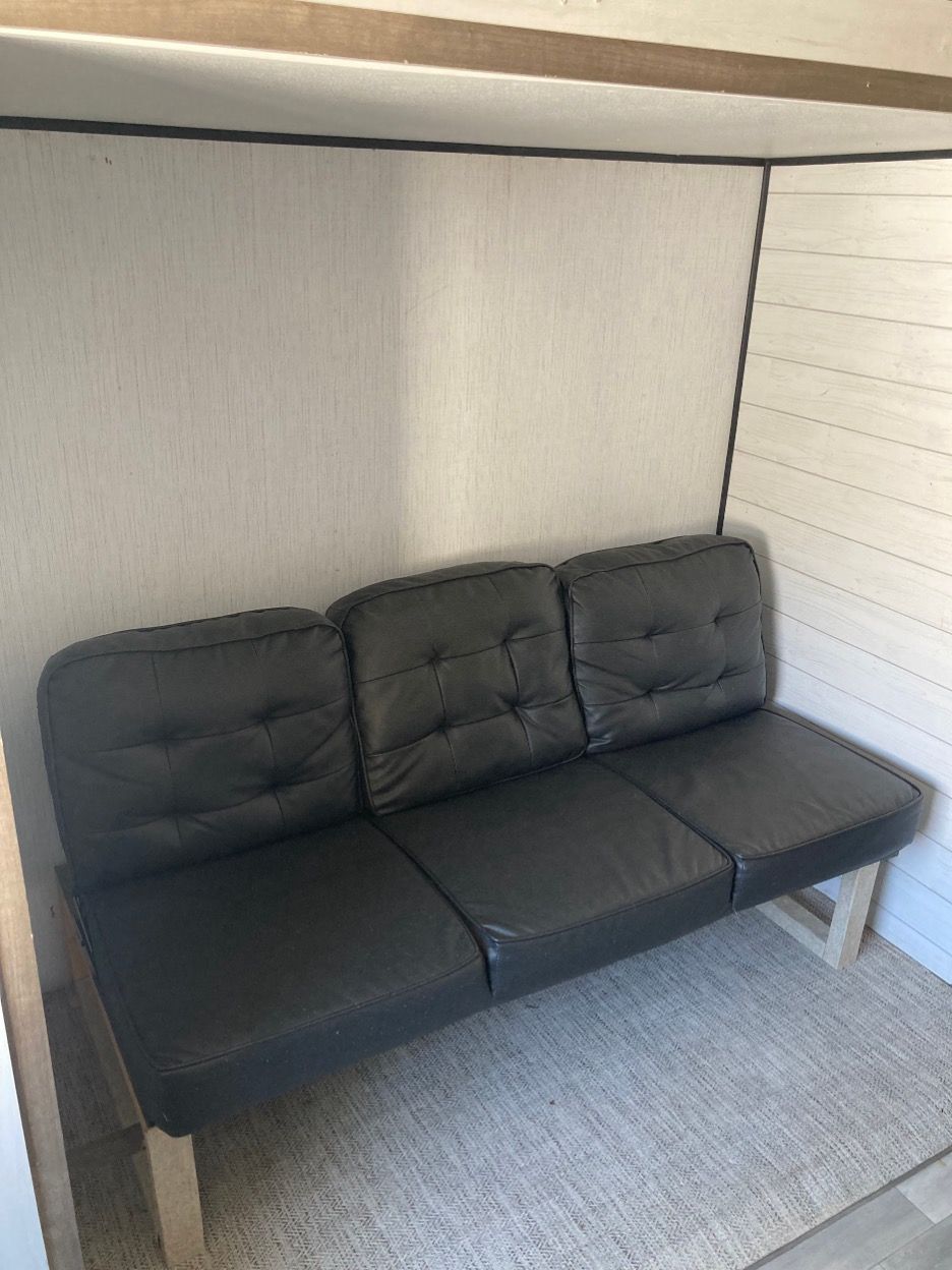 Black futon couch in a recessed nook with beige walls and a white-paneled wall.