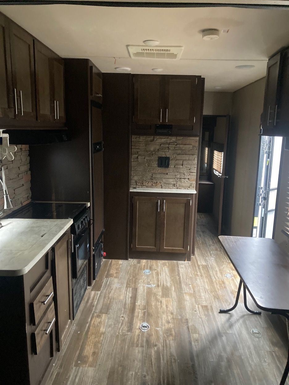 Interior of a recreational vehicle with dark brown cabinets, a kitchen, and a dining table.