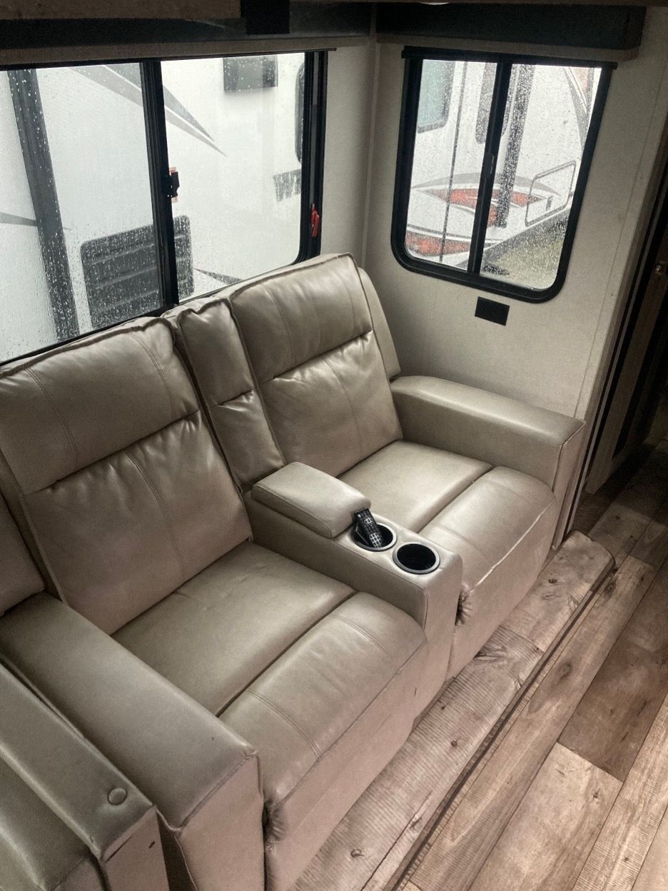 Tan leather RV recliner seats with cupholders, near windows.