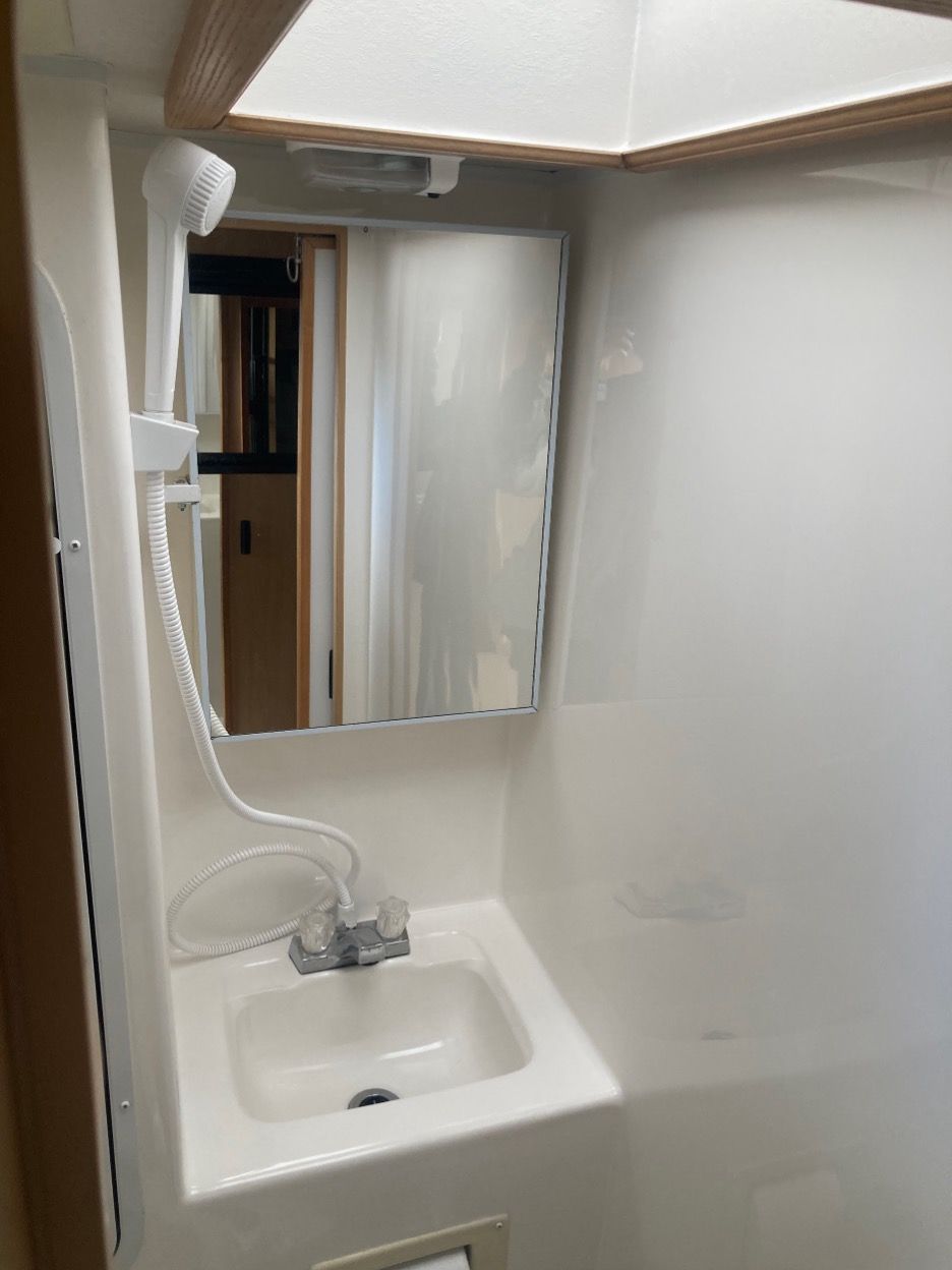 Small RV bathroom with sink, mirror, shower, and skylight. White surfaces.