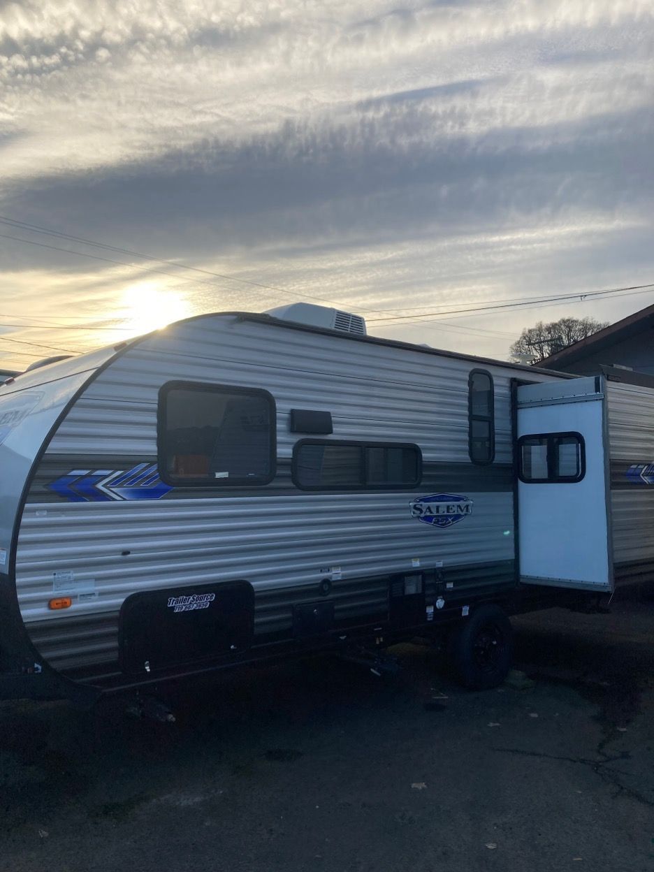 Silver travel trailer with blue accents parked outdoors under a cloudy sky.