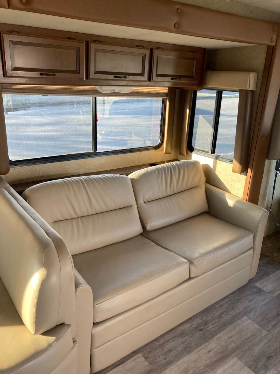 Beige couch in an RV interior with windows and overhead cabinets.