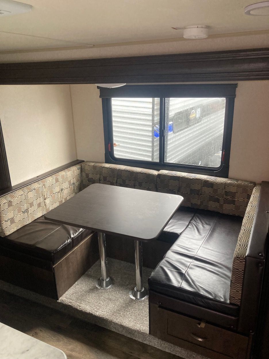 U-shaped dinette in a camper with a table, window, and dark accents.