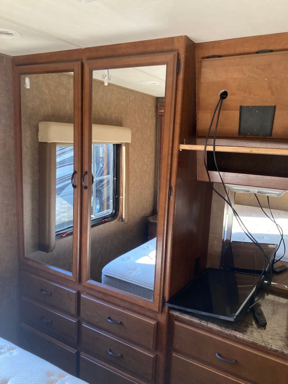 Interior RV with mirrored closet, drawers, window, and small TV on a counter.