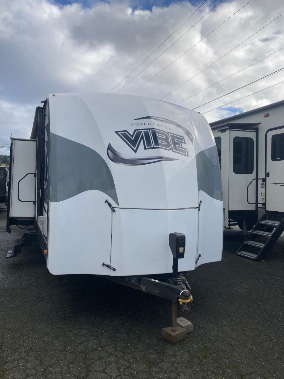 White and gray Vibe travel trailer with a hitch, parked outside.
