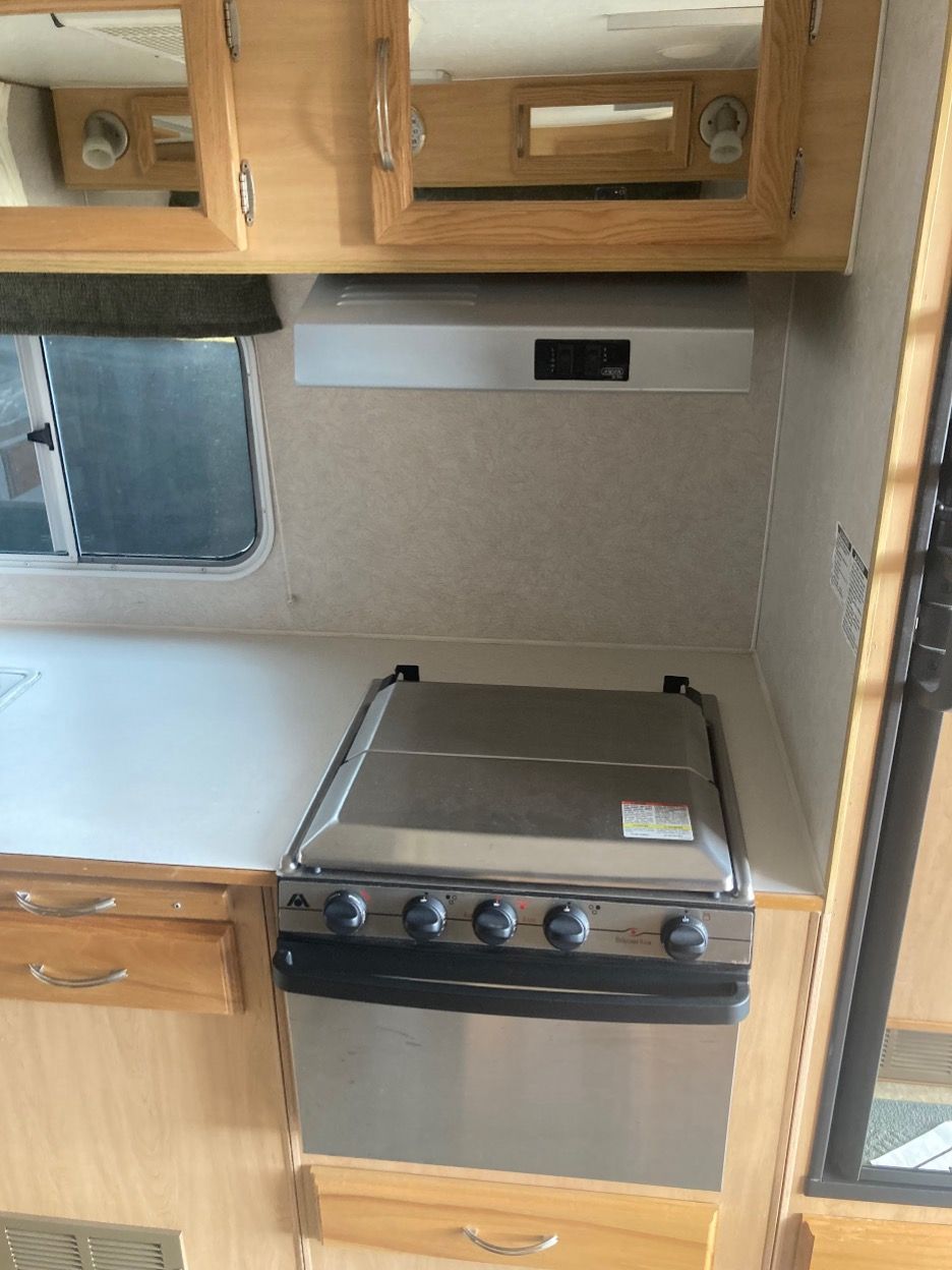 RV kitchen with stainless steel stove, cabinets, and vent hood.