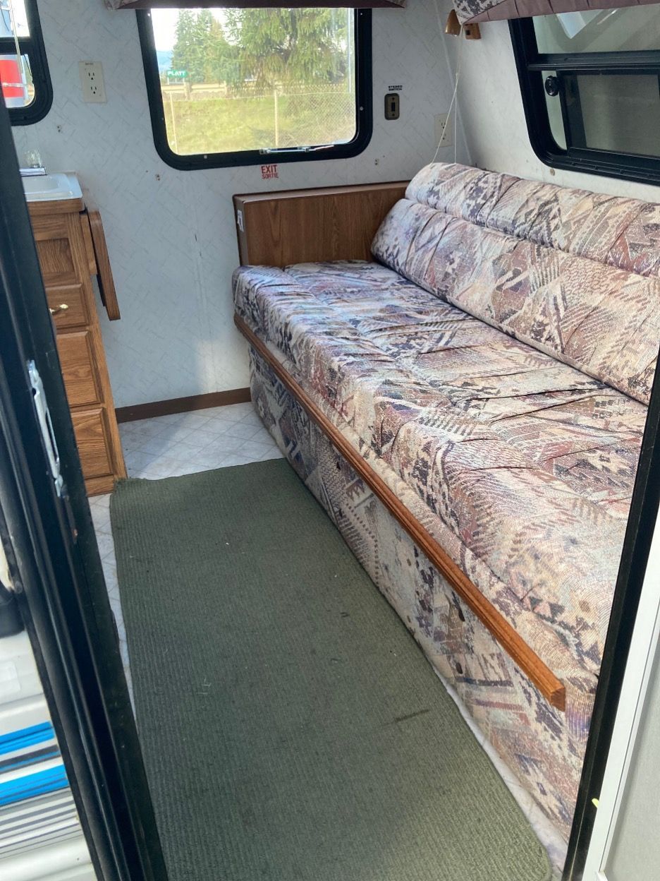 Interior of a small camper, featuring a patterned sofa, a window, and a small cabinet.