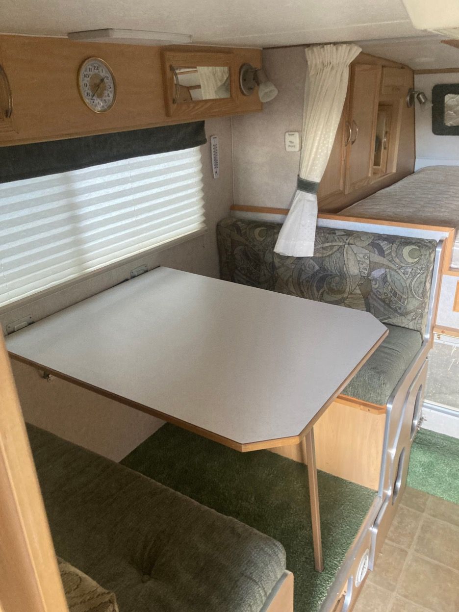 Interior of a camper with a table and seating area, cabinets, and a bed.