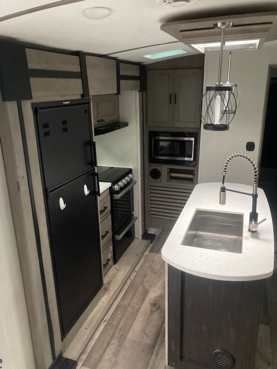 RV kitchen with a refrigerator, stove, microwave, and sink.