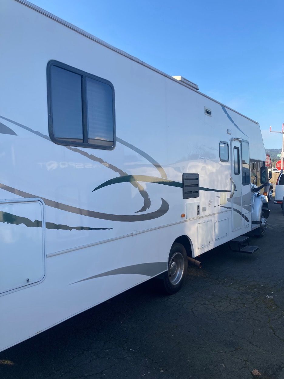 White RV with gray and green design parked outdoors on asphalt.