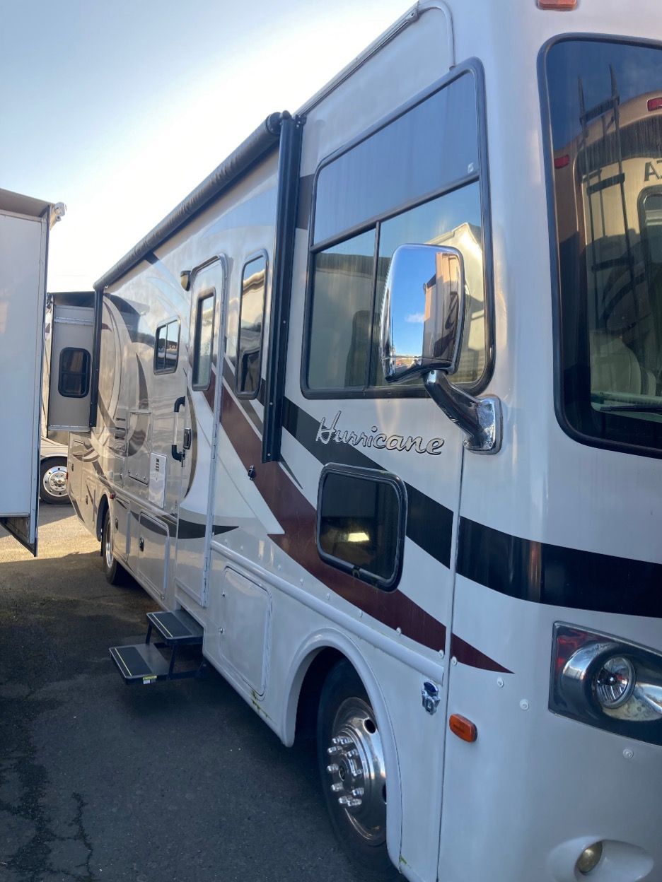 White RV parked outside, side view, awning extended, brown and black accent stripes.