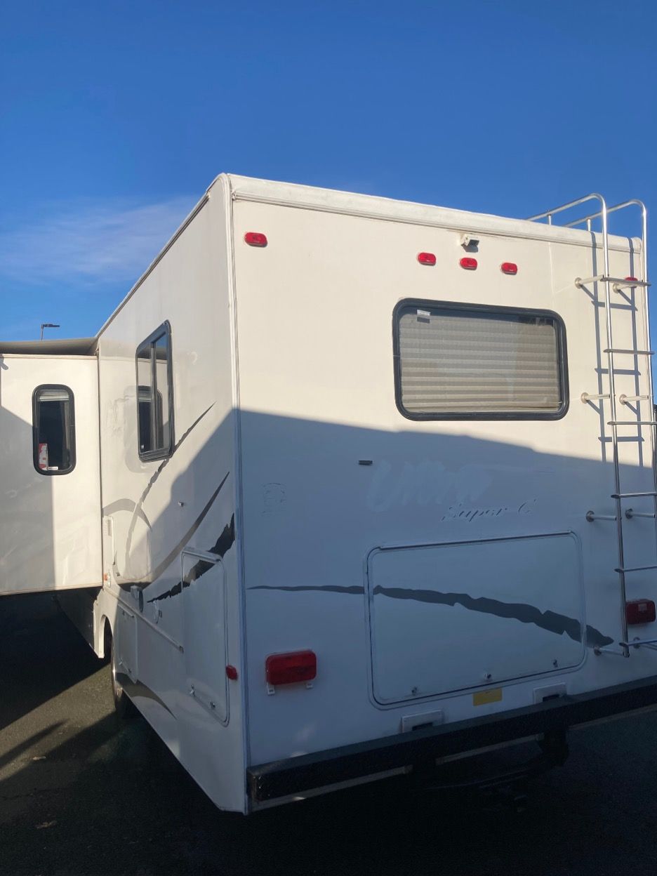 White RV with ladder, windows, and black accents against a blue sky.