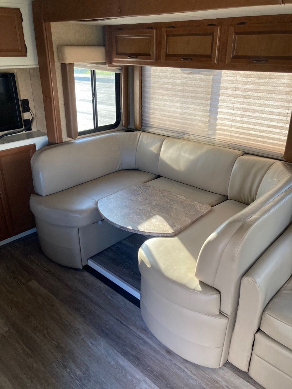 Interior view of an RV with a tan U-shaped booth, round table, and a window.