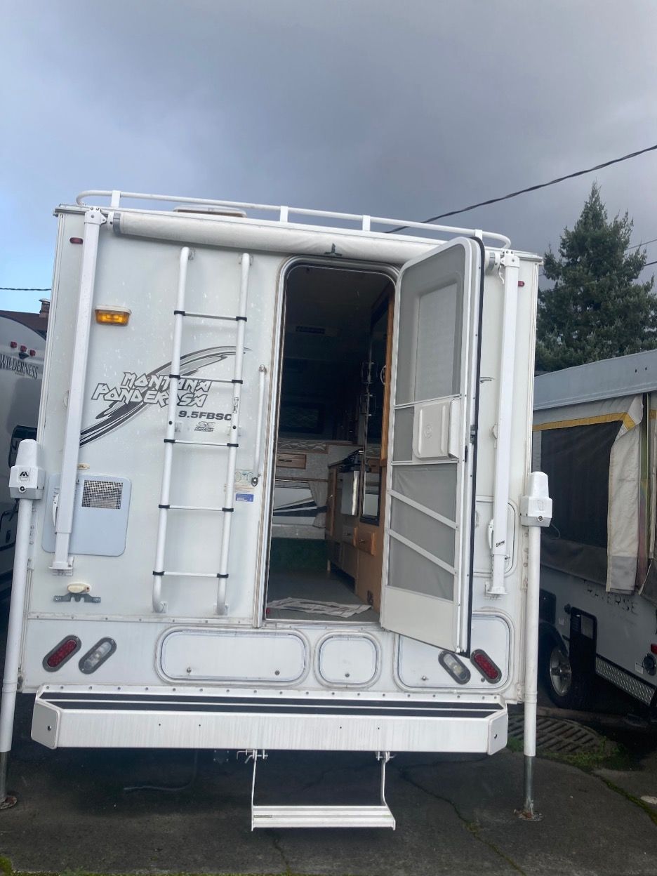 White camper trailer with open door, ladder, and step on a driveway.