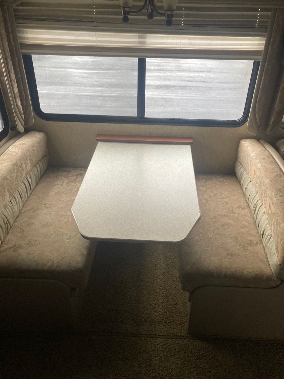A dinette area inside a recreational vehicle, with a table and cushioned bench seats in front of a window.