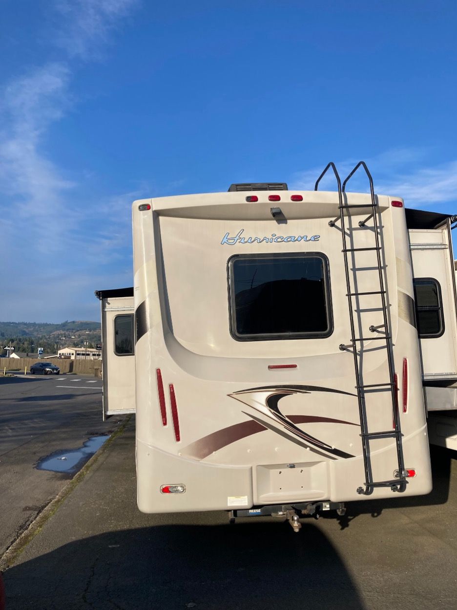 White and brown RV, rear view, with ladder. 