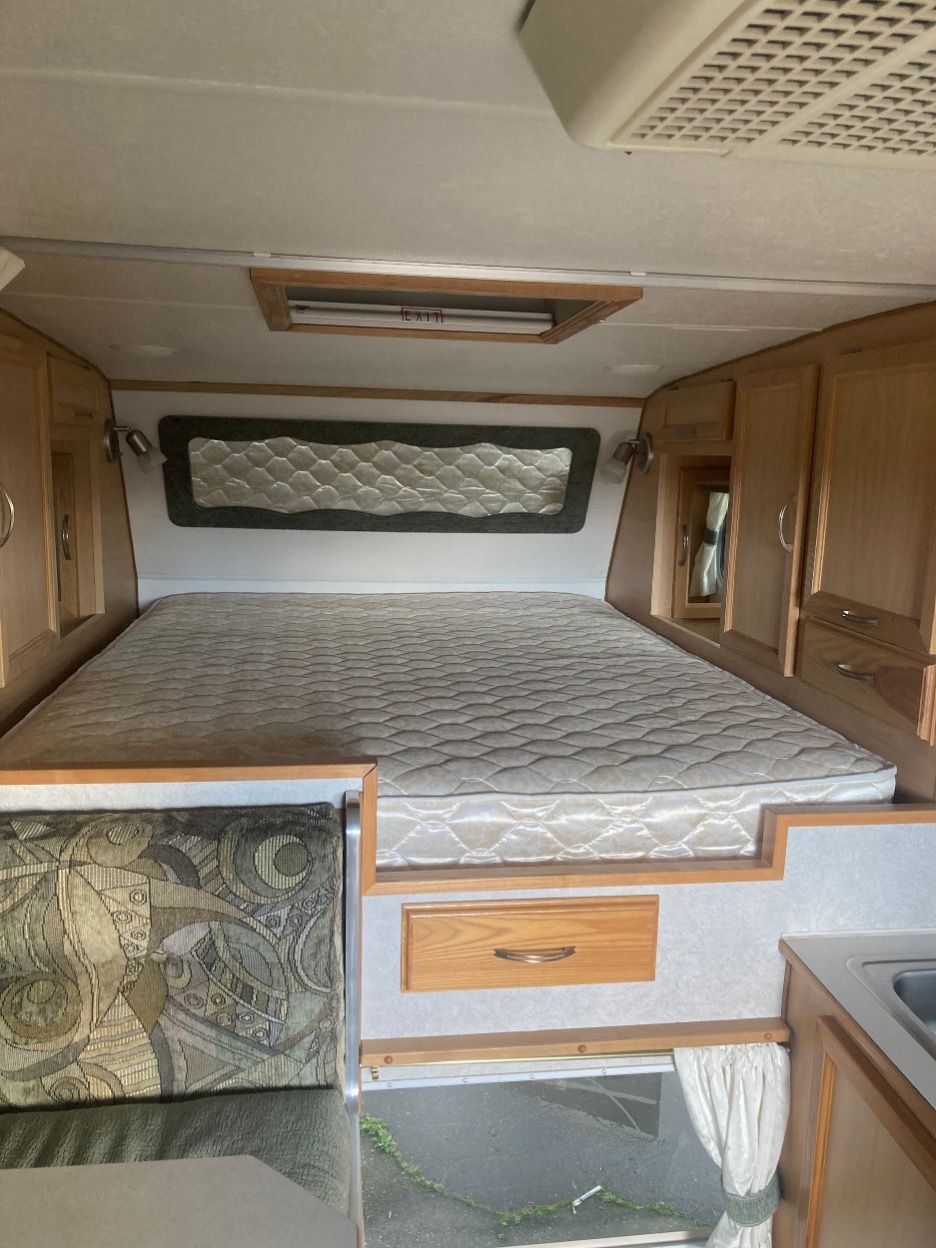 Interior of a camper with a bed, cabinets, and a ceiling vent.