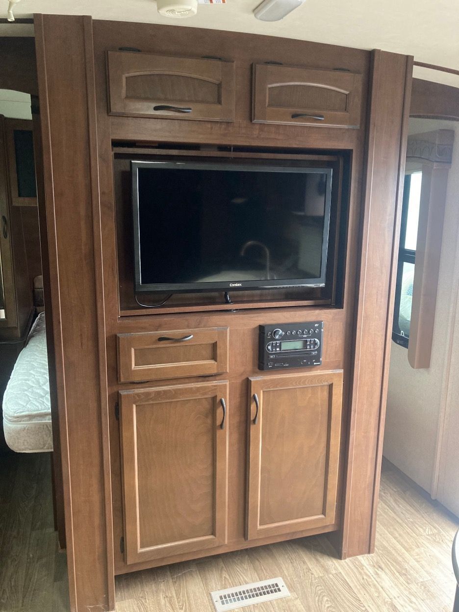 RV interior with built-in cabinetry, TV, stereo, and storage. Brown wood, neutral tones.