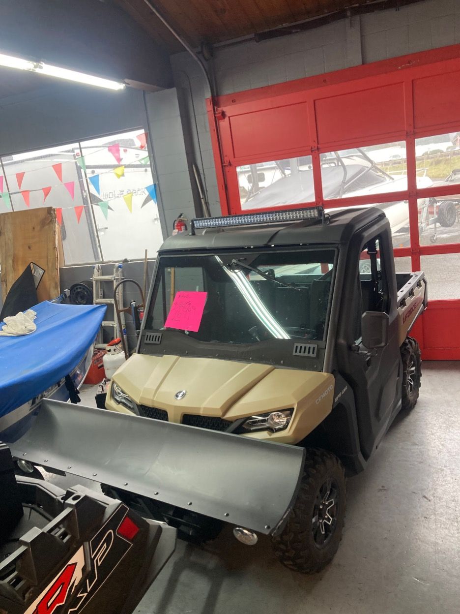 Tan utility vehicle with snow plow in a garage with red doors and a light bar.