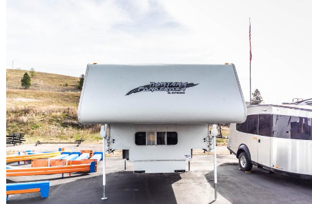 White truck camper parked on asphalt; mountain in background.