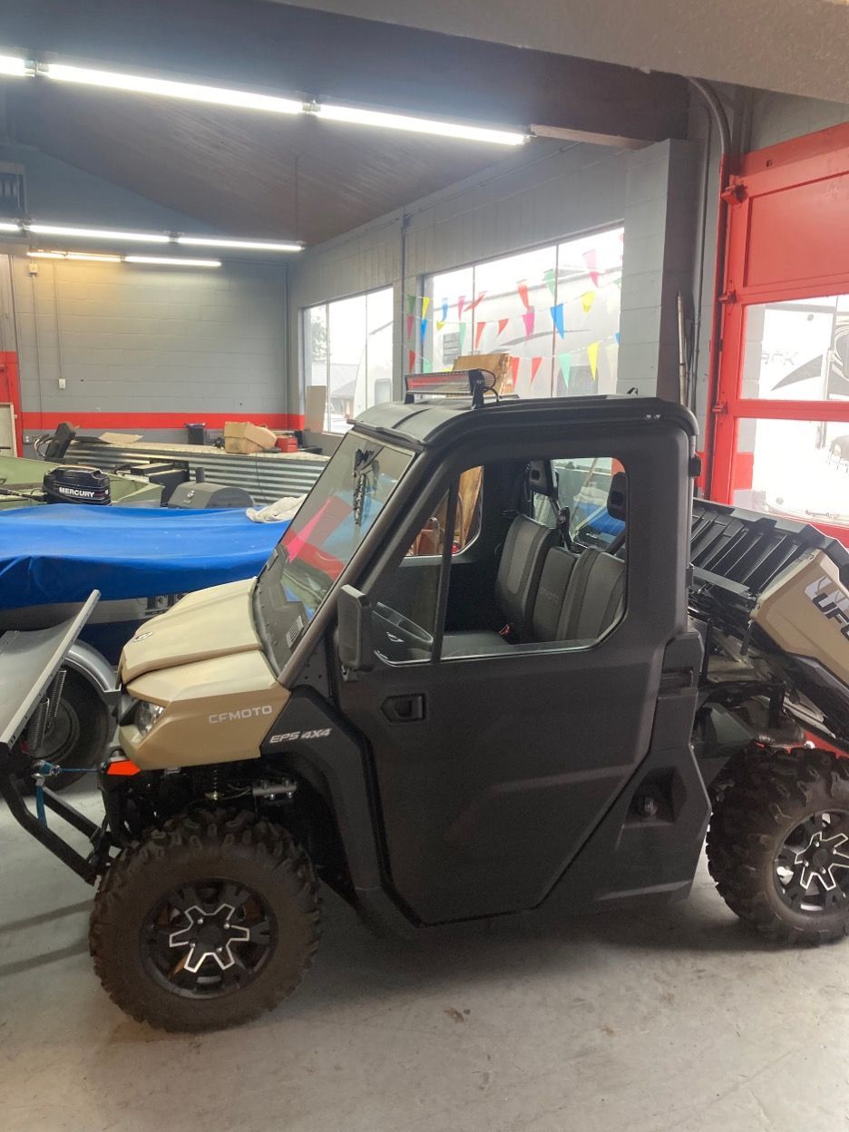 Tan and black side-by-side utility vehicle inside a garage. It has black doors and tires.