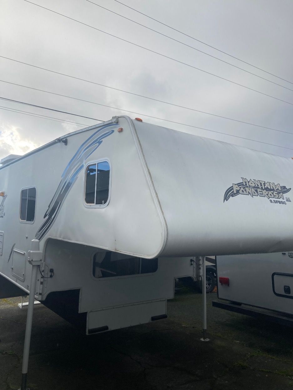 White truck camper with windows and graphic details, parked outdoors under a cloudy sky.