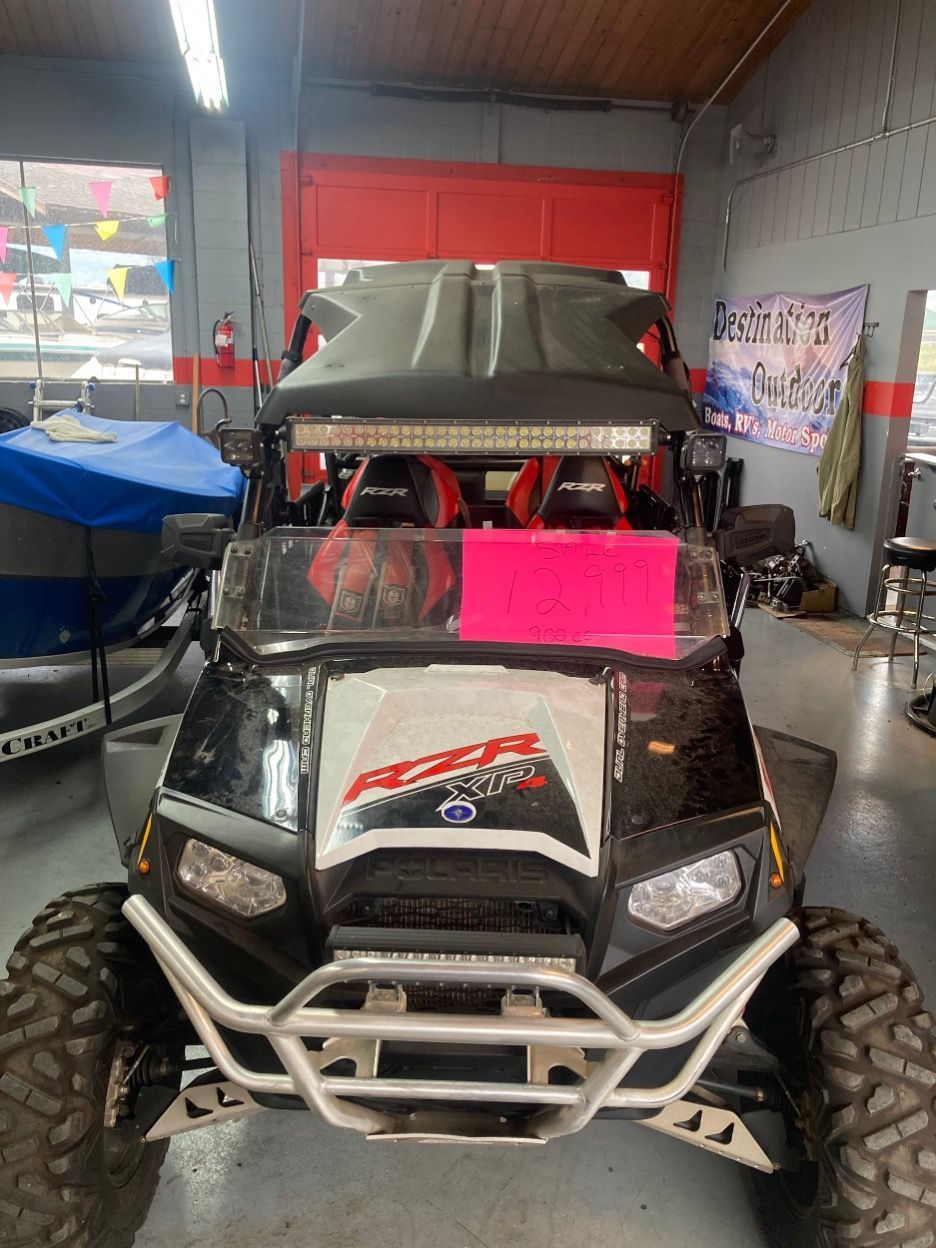 Black Polaris RZR side-by-side UTV with light bar and windshield, parked indoors.