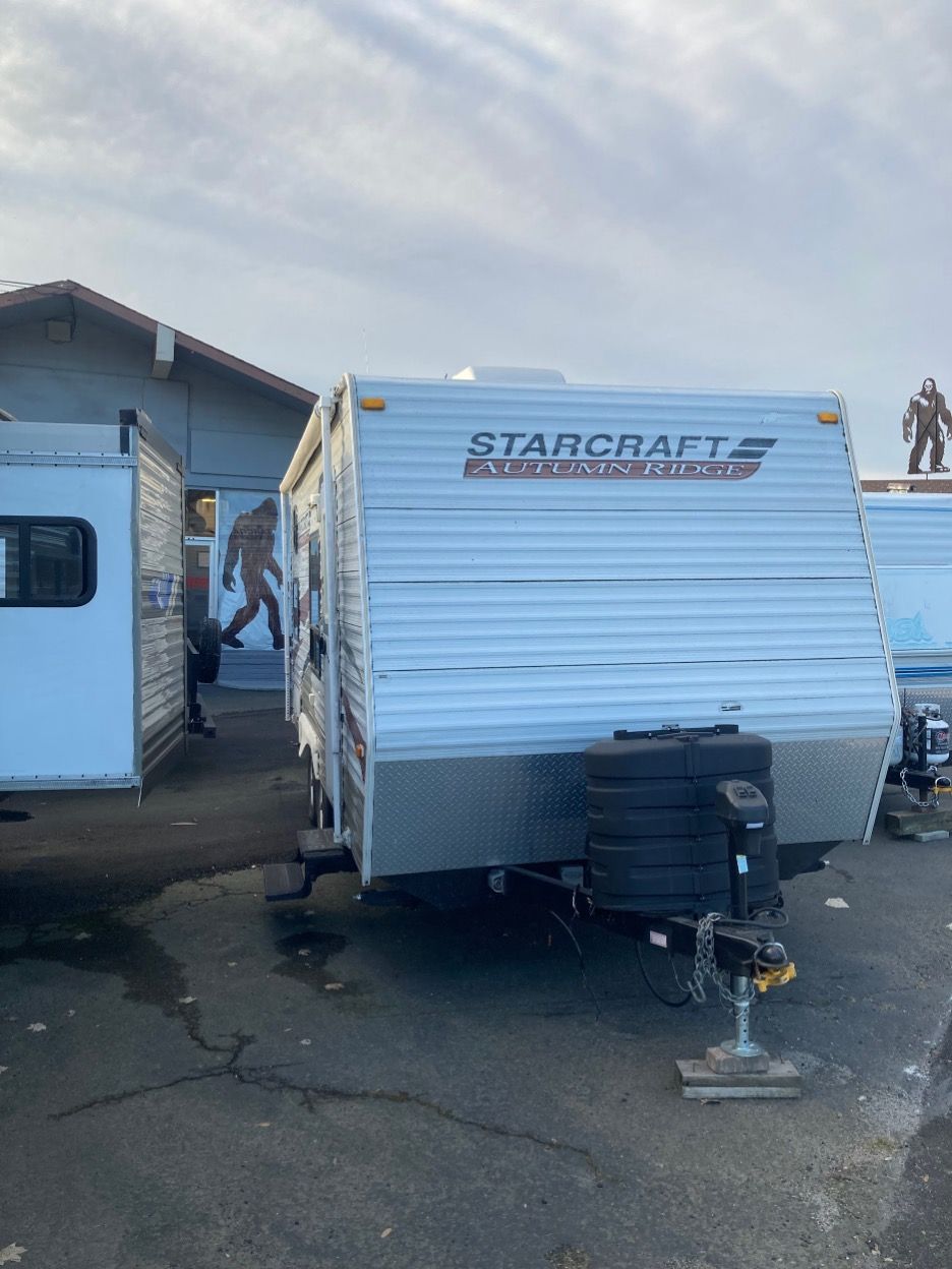 A white Starcraft camper trailer parked outside on asphalt. A building and another trailer are visible.