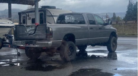 A gray Dodge Ram truck on blocks is parked in front of a camper. The truck is hooked up to a trailer.