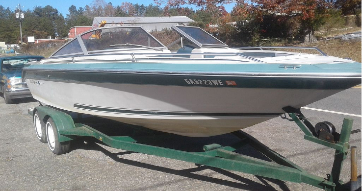 Boat on a trailer, teal and white, parked outside.