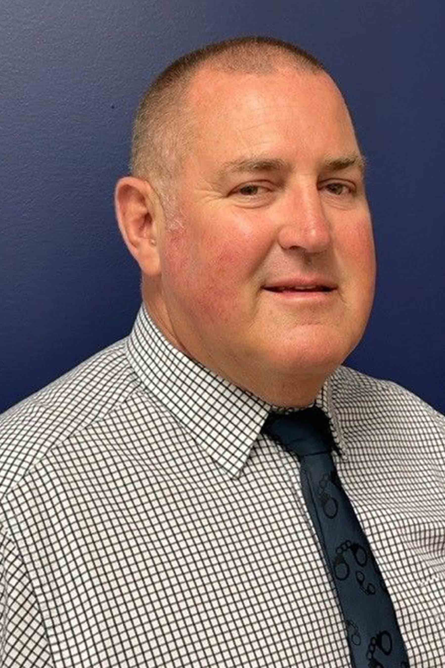A man in a plaid shirt and tie is smiling for the camera.