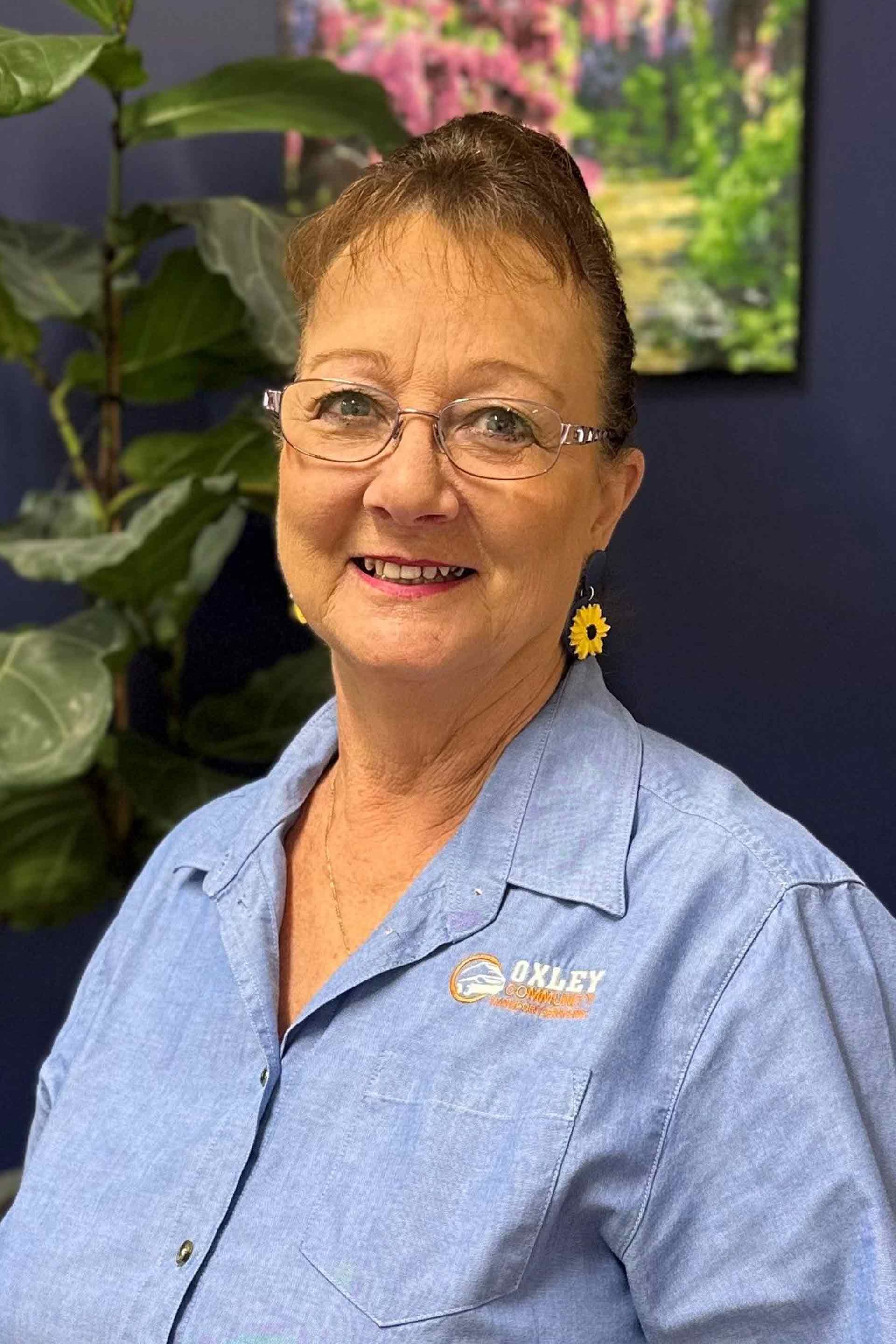 A woman wearing glasses and a blue shirt is smiling for the camera.