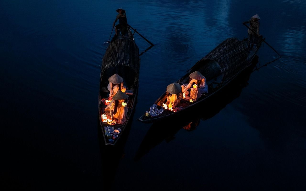 2 boats on a lake, with people on them, wearing traditional Chinese hats and holding lighted candles