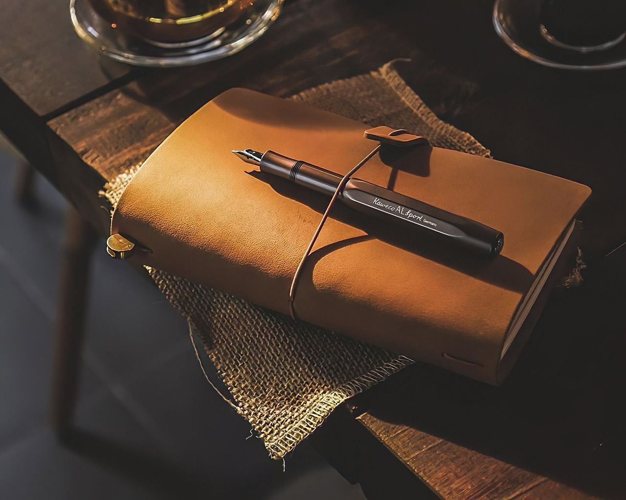 Picture of a notebook covered in leather, with a pen over it