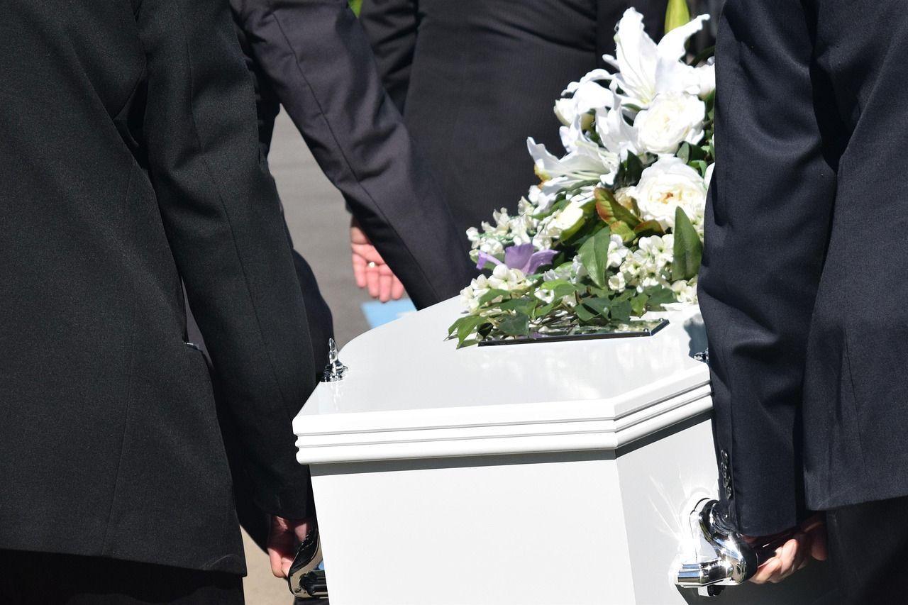white casket being carried by men, with flowers on top