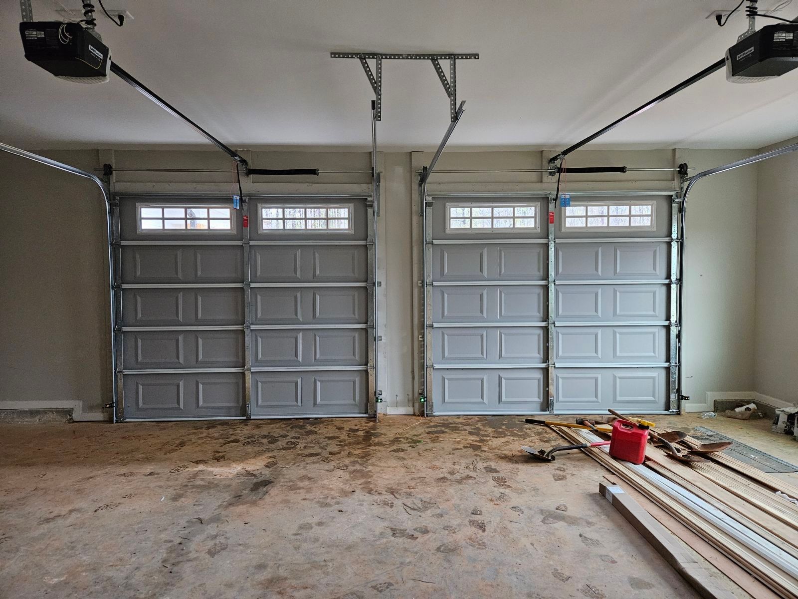 A garage with two garage doors open and a red bucket on the floor.