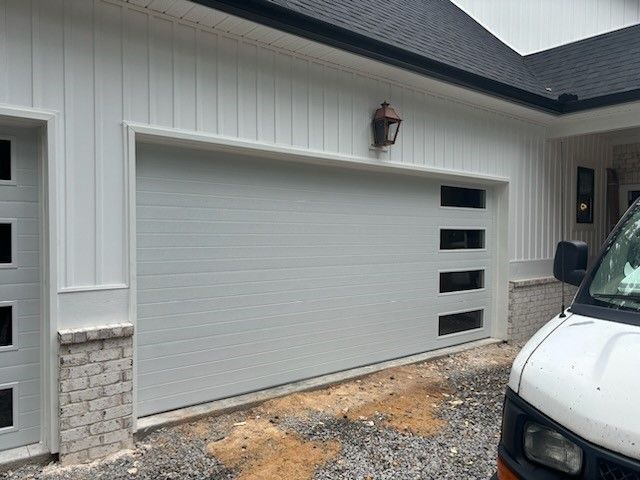 A white van is parked in front of a white garage door.