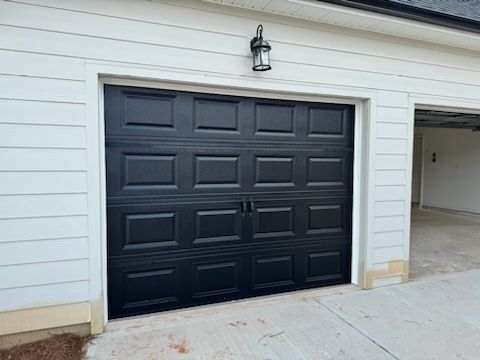 A black garage door is sitting in front of a white house.