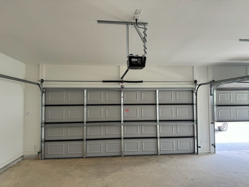 An empty garage with a garage door open and a garage door opener hanging from the ceiling.