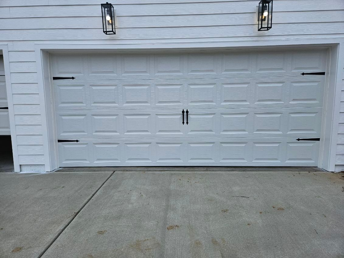 A white garage door is sitting on the side of a white house.