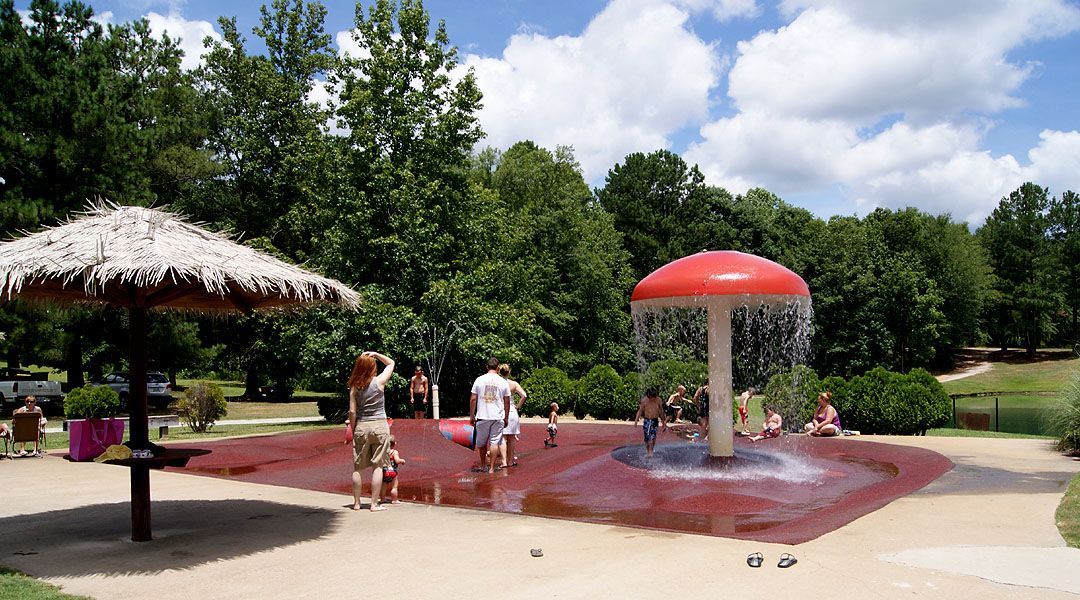 A group of people are playing in a water fountain in a park in Carrollton ga.