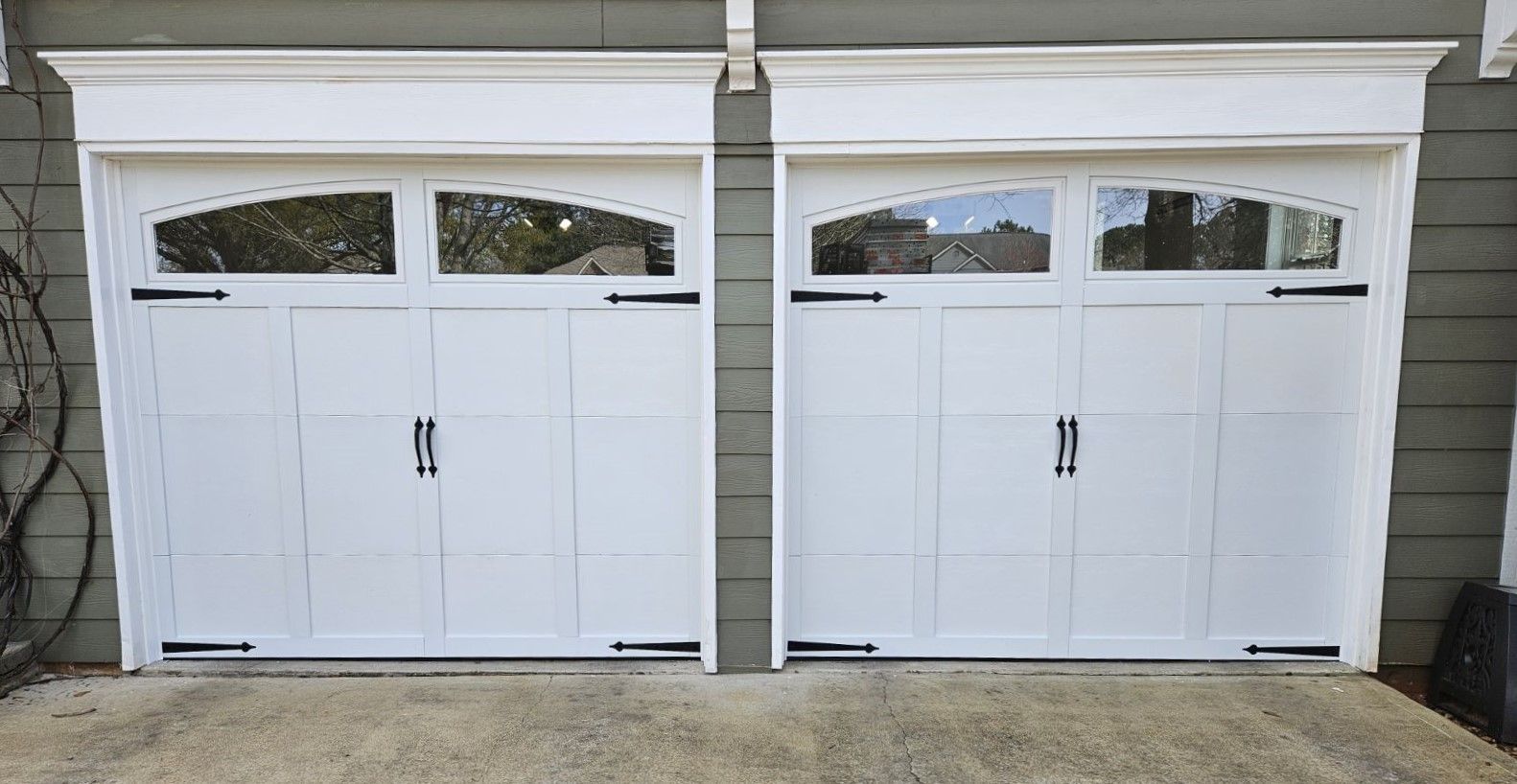 Two white garage doors are sitting next to each other on the side of a house.