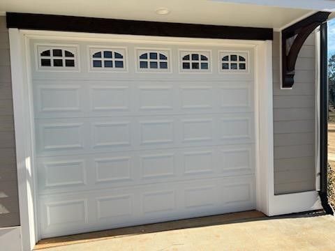 A white garage door with windows on it is sitting on the side of a house.