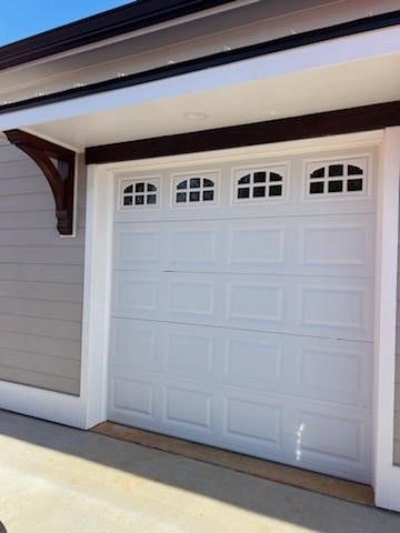A white garage door with windows on it is on the side of a house.